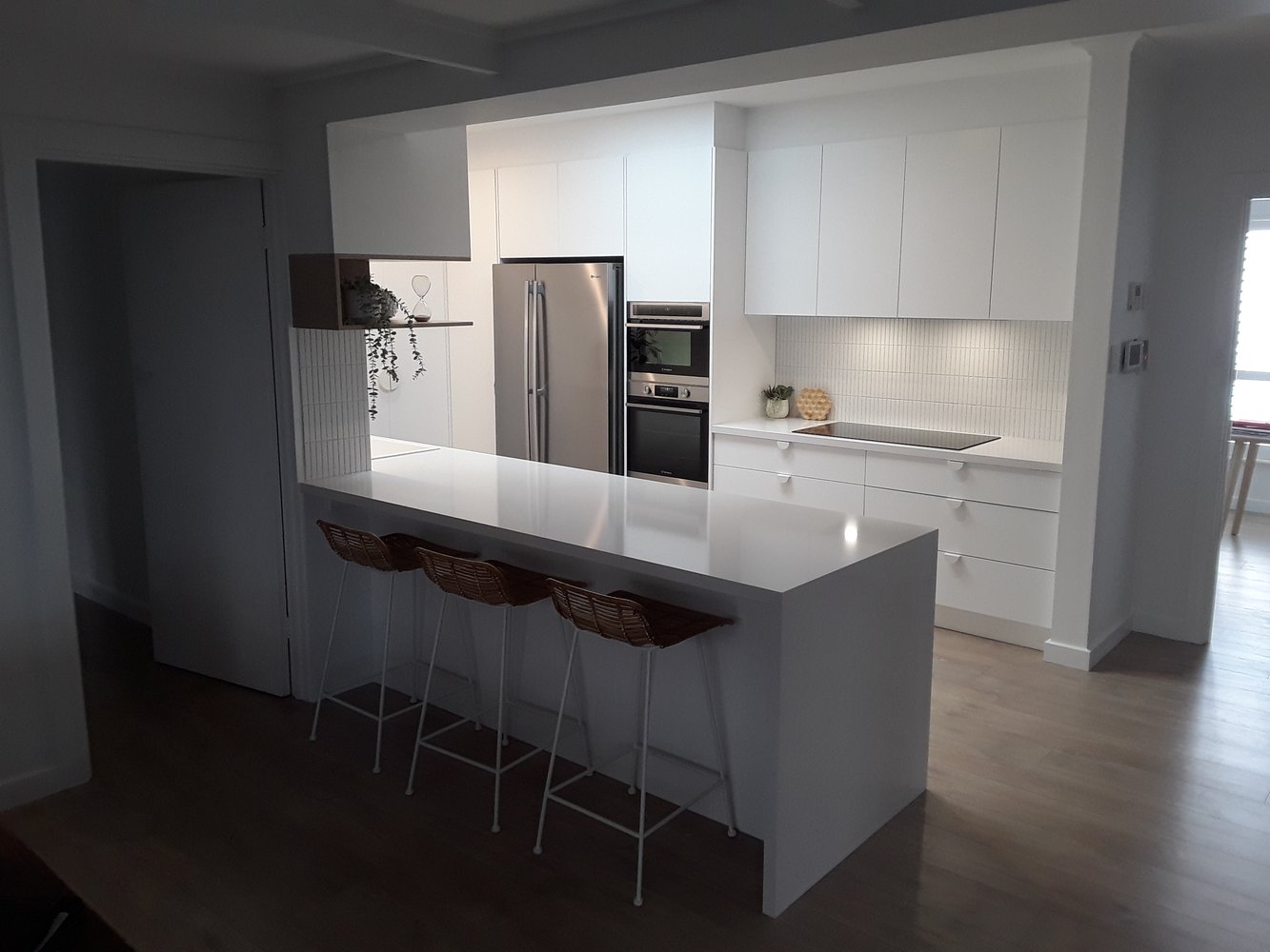 Modern white kitchen renovation with island and rattan stools